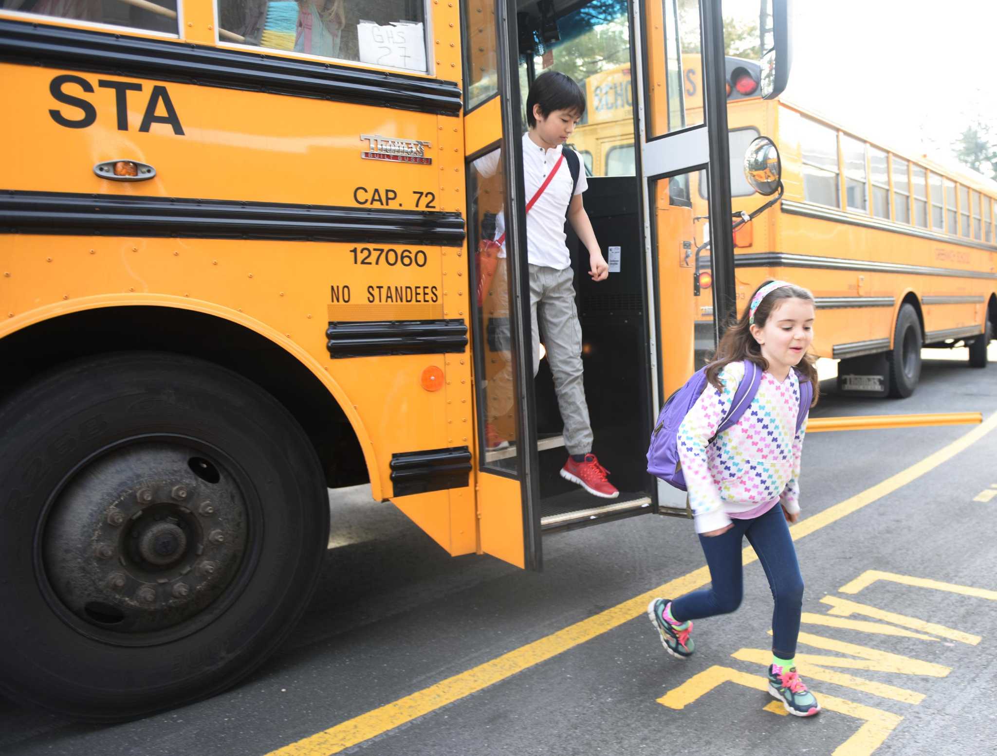 Fifth-grader Koto Freeman, left, and kindergartener Sophia Sinclair get off the school bus at North Street School in Greenwich, Conn. Thursday, March 10, 2016. State legislation has been proposed to require seat belts on all school buses.